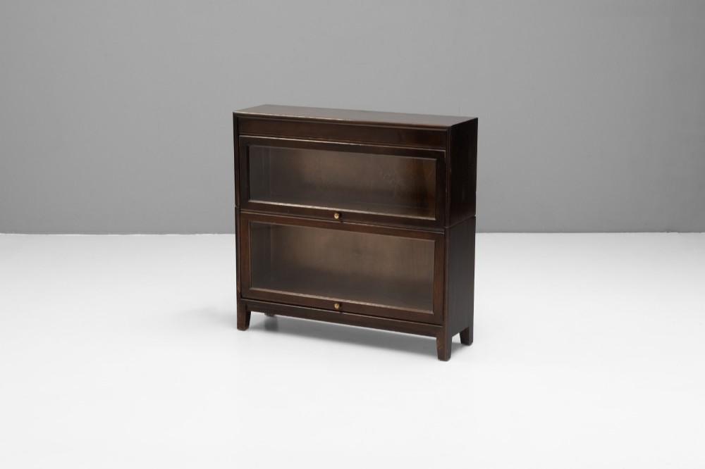 A four-tier dark wood sectional bookcase featuring glazed lift-and-slide doors with central brass knobs. View XI