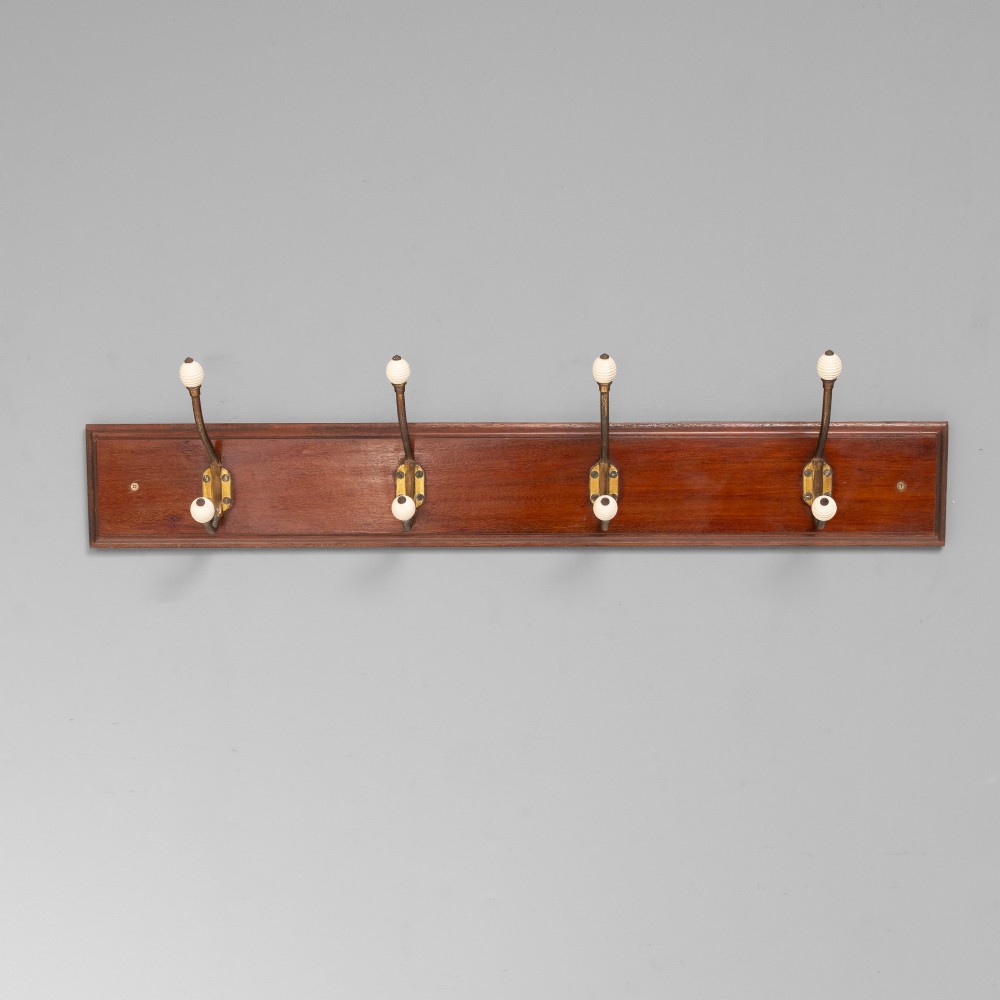 A Victorian wall-mounted mahogany coat rack featuring four brass hooks with white ceramic knobs set against a rectangular wooden backboard. View II
