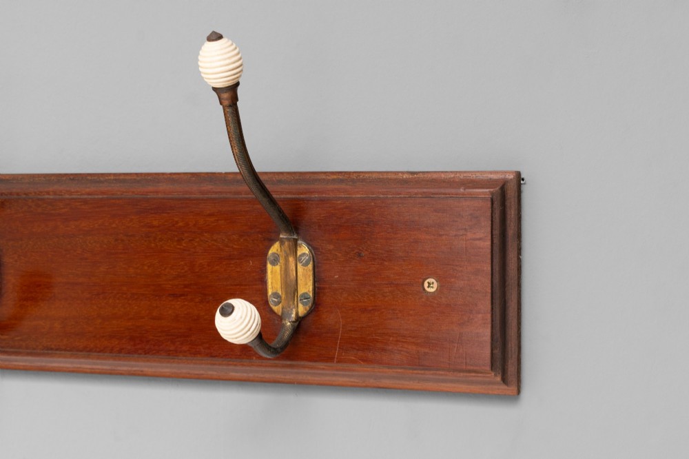 A Victorian wall-mounted mahogany coat rack featuring four brass hooks with white ceramic knobs set against a rectangular wooden backboard. View III