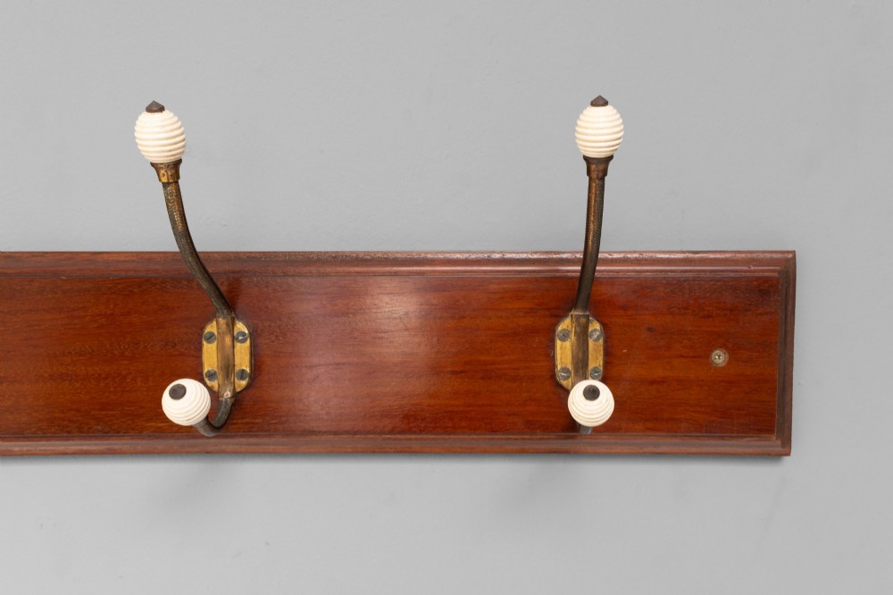 A Victorian wall-mounted mahogany coat rack featuring four brass hooks with white ceramic knobs set against a rectangular wooden backboard. View IV