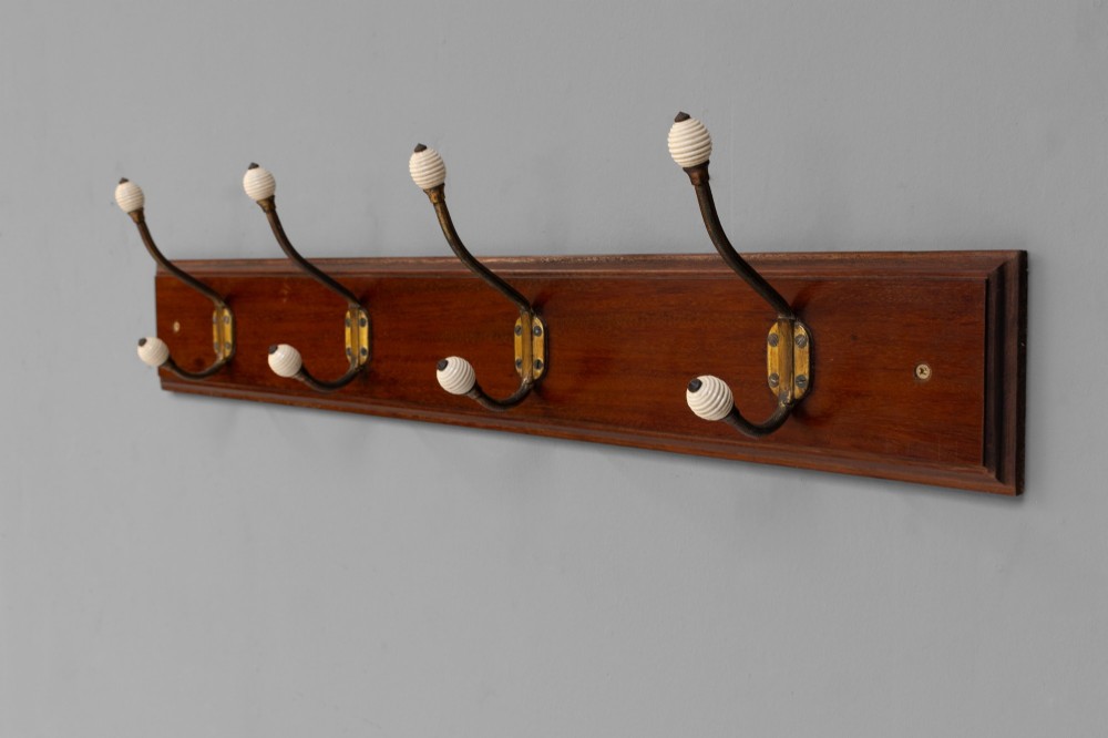 A Victorian wall-mounted mahogany coat rack featuring four brass hooks with white ceramic knobs set against a rectangular wooden backboard. View V