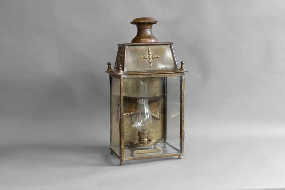 An antique glazed brass and copper lantern housing an internal glass oil lamp chimney and burner against a polished backplate. View II