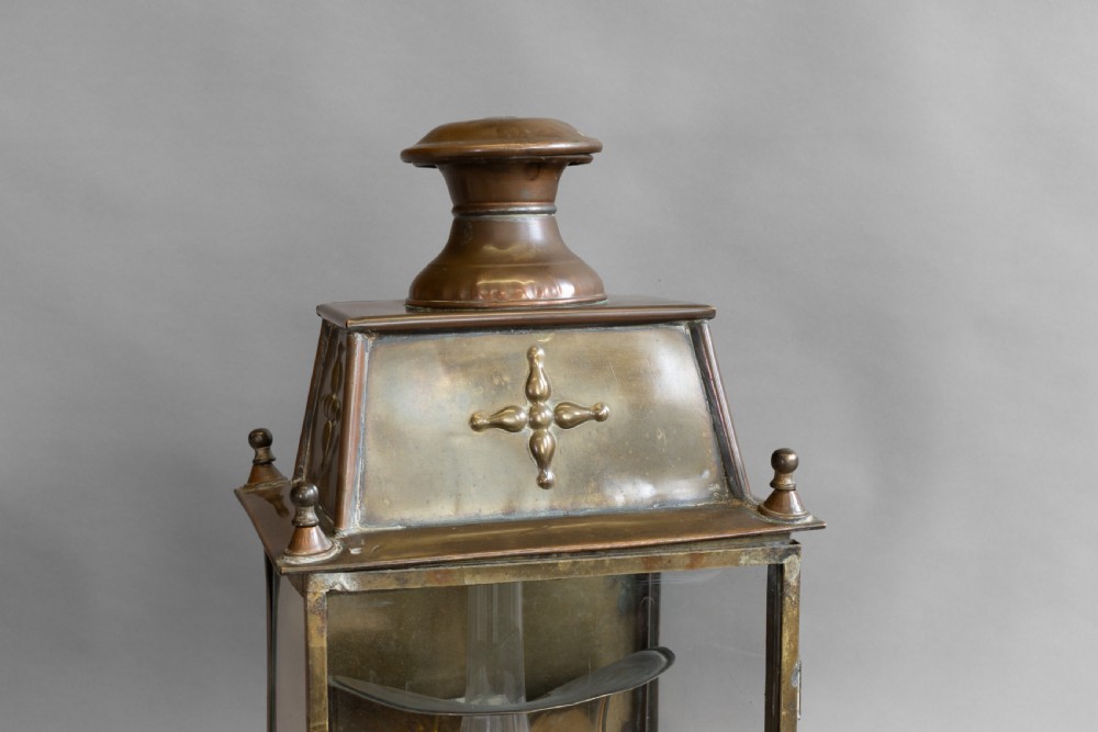 An antique glazed brass and copper lantern housing an internal glass oil lamp chimney and burner against a polished backplate. View IV
