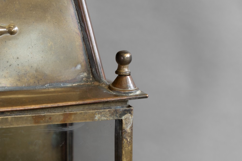 An antique glazed brass and copper lantern housing an internal glass oil lamp chimney and burner against a polished backplate. View V