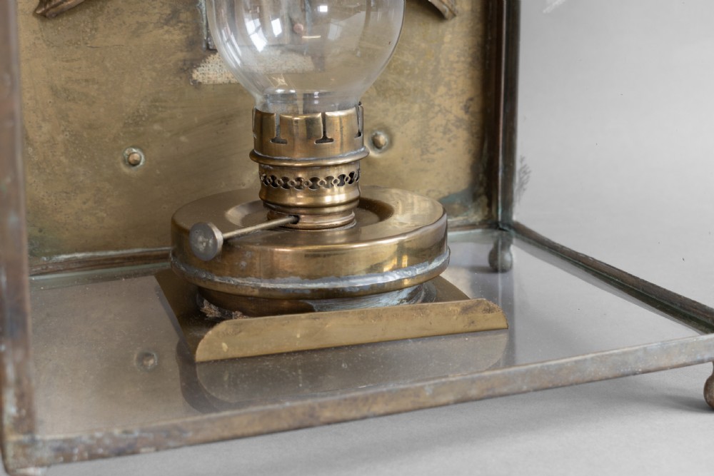 An antique glazed brass and copper lantern housing an internal glass oil lamp chimney and burner against a polished backplate. View VI