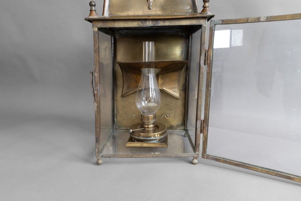 An antique glazed brass and copper lantern housing an internal glass oil lamp chimney and burner against a polished backplate. View VII