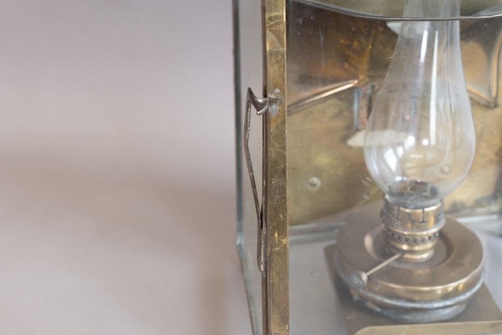 An antique glazed brass and copper lantern housing an internal glass oil lamp chimney and burner against a polished backplate. View IX