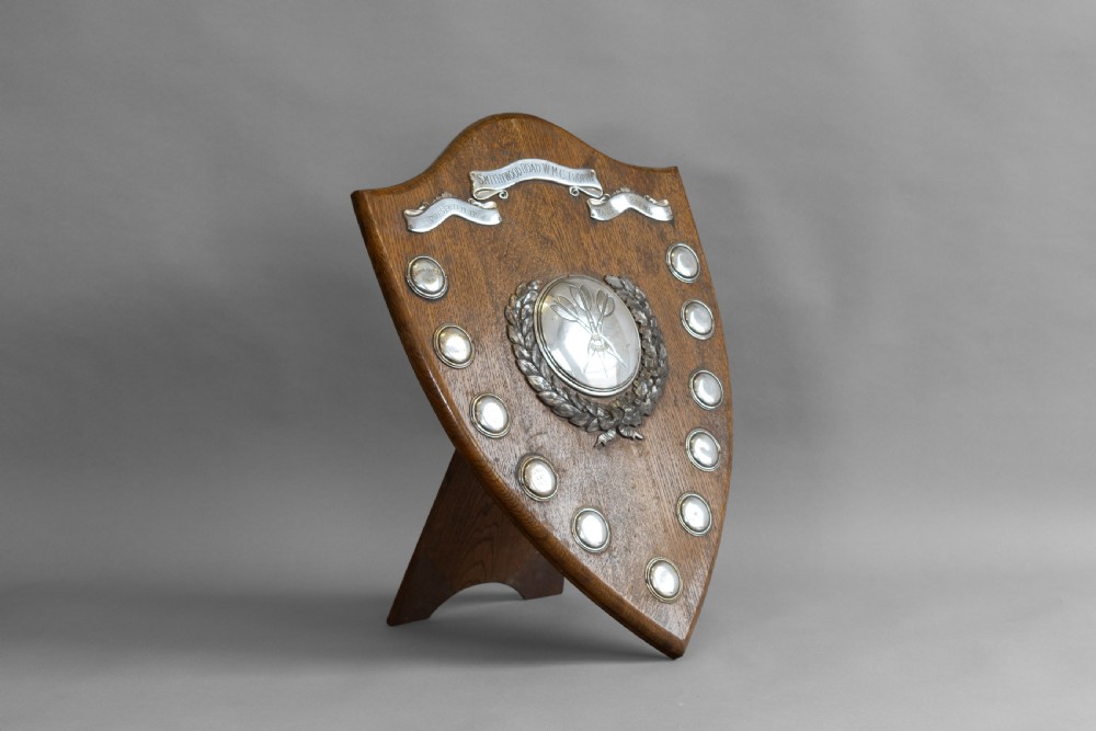 A standing shield-shaped oak presentation trophy featuring an oval silver darts motif surrounded by small silver winner plaques. View II
