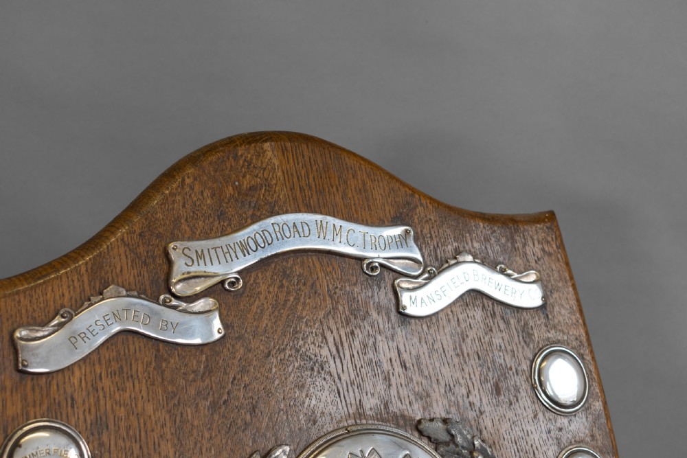 A standing shield-shaped oak presentation trophy featuring an oval silver darts motif surrounded by small silver winner plaques. View III