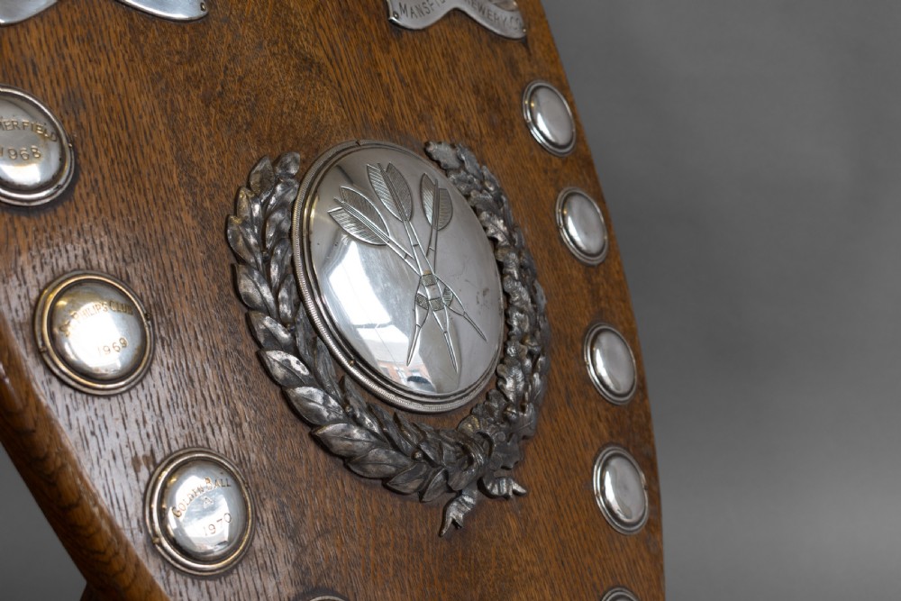 A standing shield-shaped oak presentation trophy featuring an oval silver darts motif surrounded by small silver winner plaques. View V