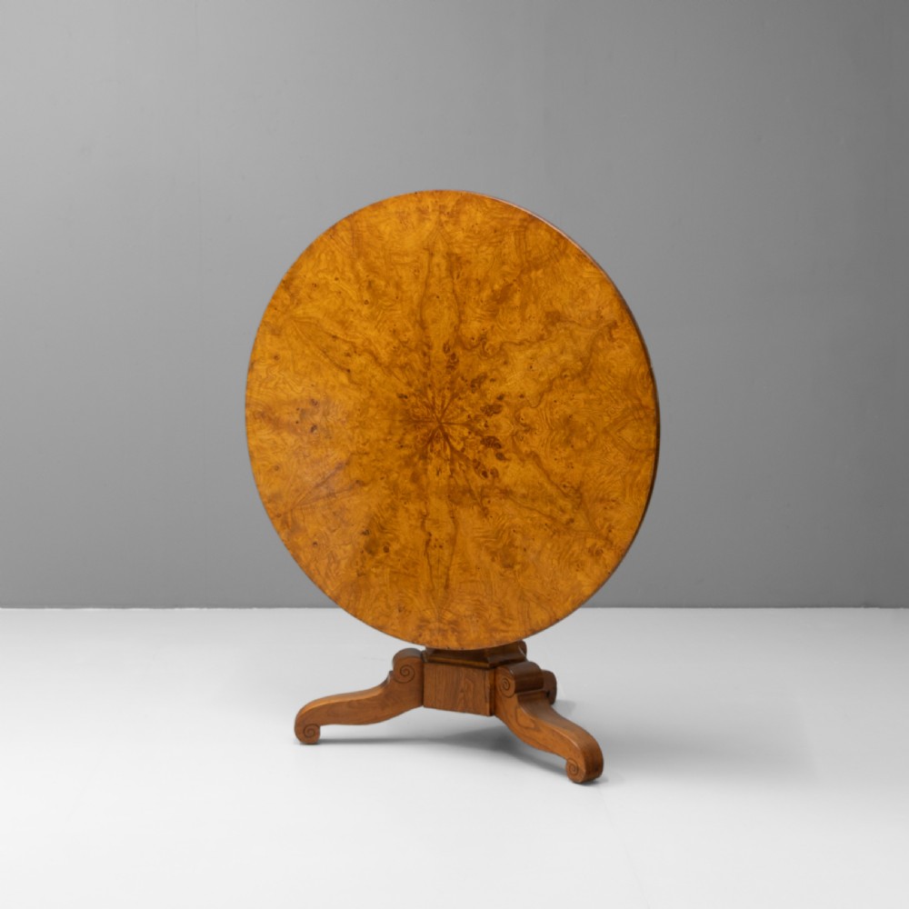 A Victorian tilt-top centre table in golden burr walnut veneer featuring a central starburst inlay and carved tripod pedestal base.
