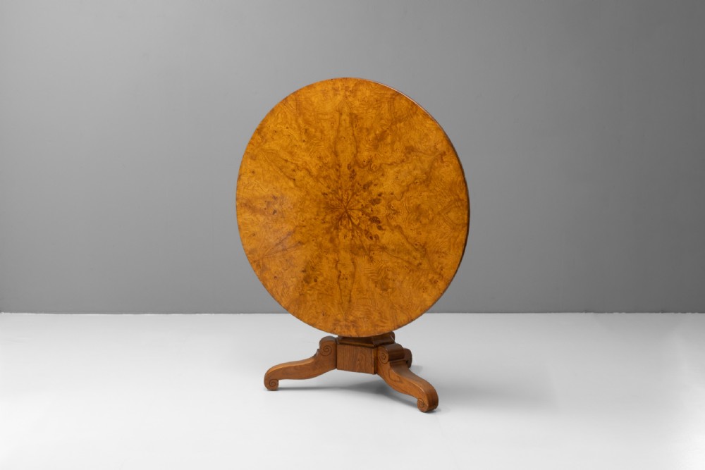 A Victorian tilt-top centre table in golden burr walnut veneer featuring a central starburst inlay and carved tripod pedestal base. View II