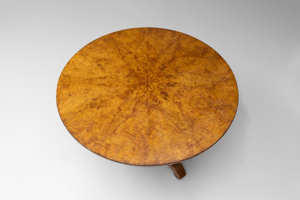 A Victorian tilt-top centre table in golden burr walnut veneer featuring a central starburst inlay and carved tripod pedestal base. View V