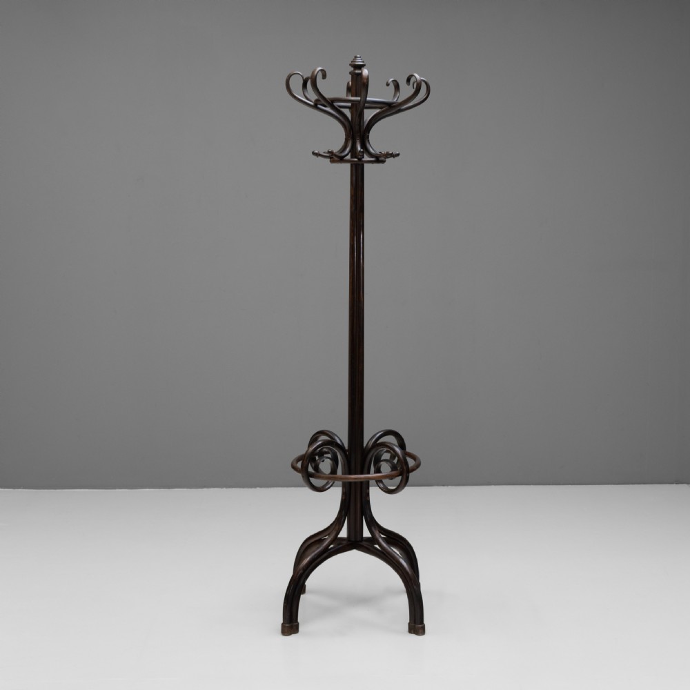 A tall dark brown bentwood coat stand with multiple S-curved hooks at the top, a slender central shaft, an integrated umbrella ring, and four curved splayed legs.