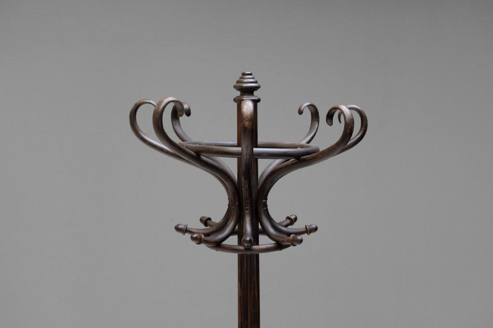 A tall dark brown bentwood coat stand with multiple S-curved hooks at the top, a slender central shaft, an integrated umbrella ring, and four curved splayed legs. View III