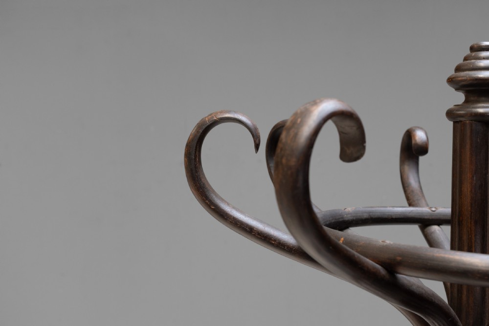 A tall dark brown bentwood coat stand with multiple S-curved hooks at the top, a slender central shaft, an integrated umbrella ring, and four curved splayed legs. View IV