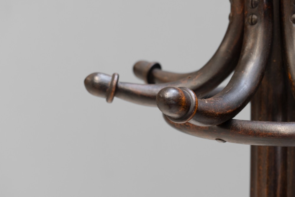 A tall dark brown bentwood coat stand with multiple S-curved hooks at the top, a slender central shaft, an integrated umbrella ring, and four curved splayed legs. View V