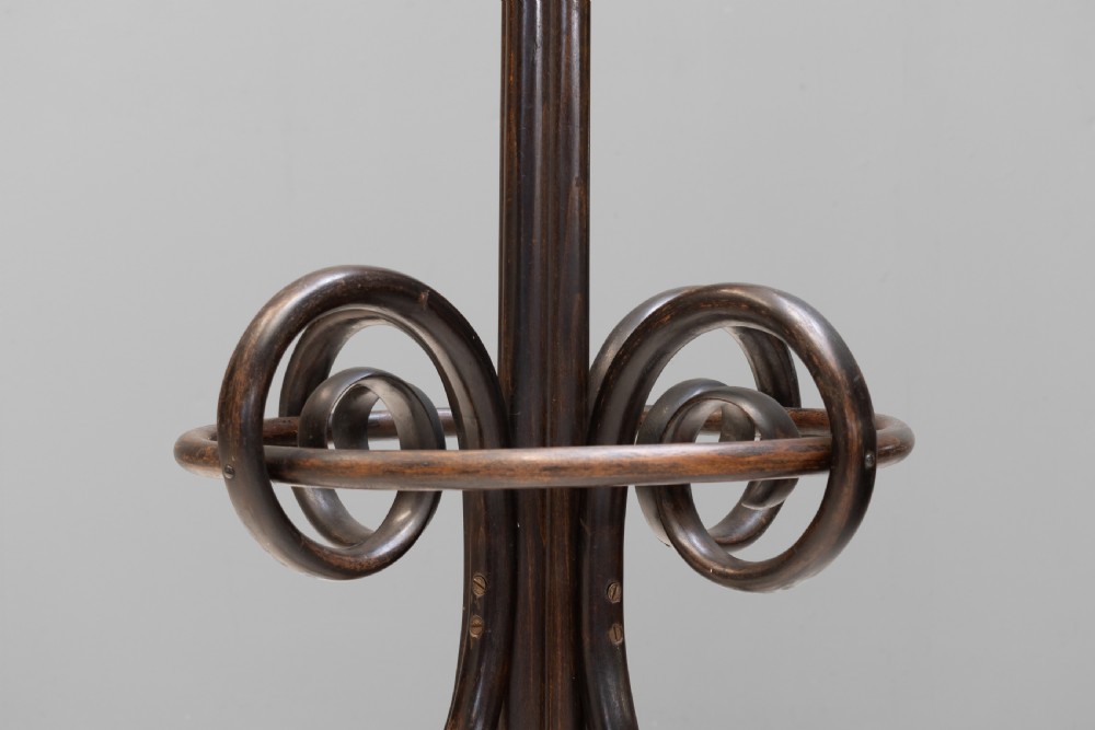 A tall dark brown bentwood coat stand with multiple S-curved hooks at the top, a slender central shaft, an integrated umbrella ring, and four curved splayed legs. View VII