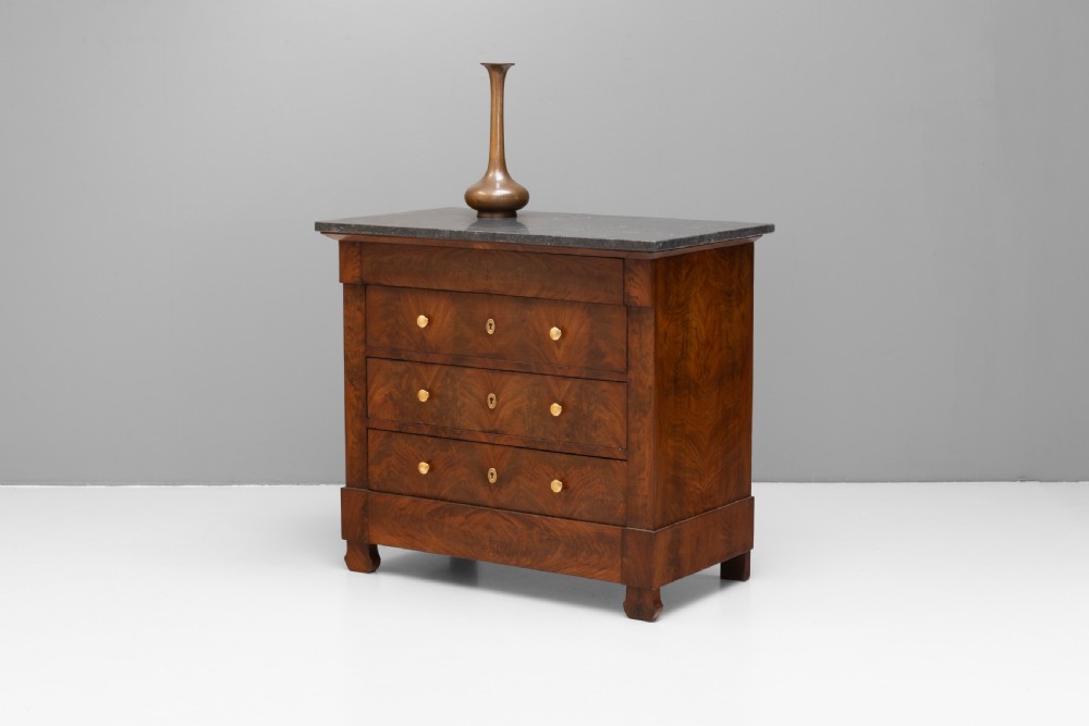 An antique 19th-century French flame walnut commode fitted with a dark grey marble slab top and brass drawer pulls.