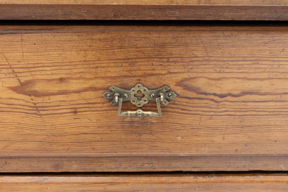 A warm brown pine sideboard featuring a central arched cupboard door flanked by six drawers with brass handles on a solid plinth base. View IX