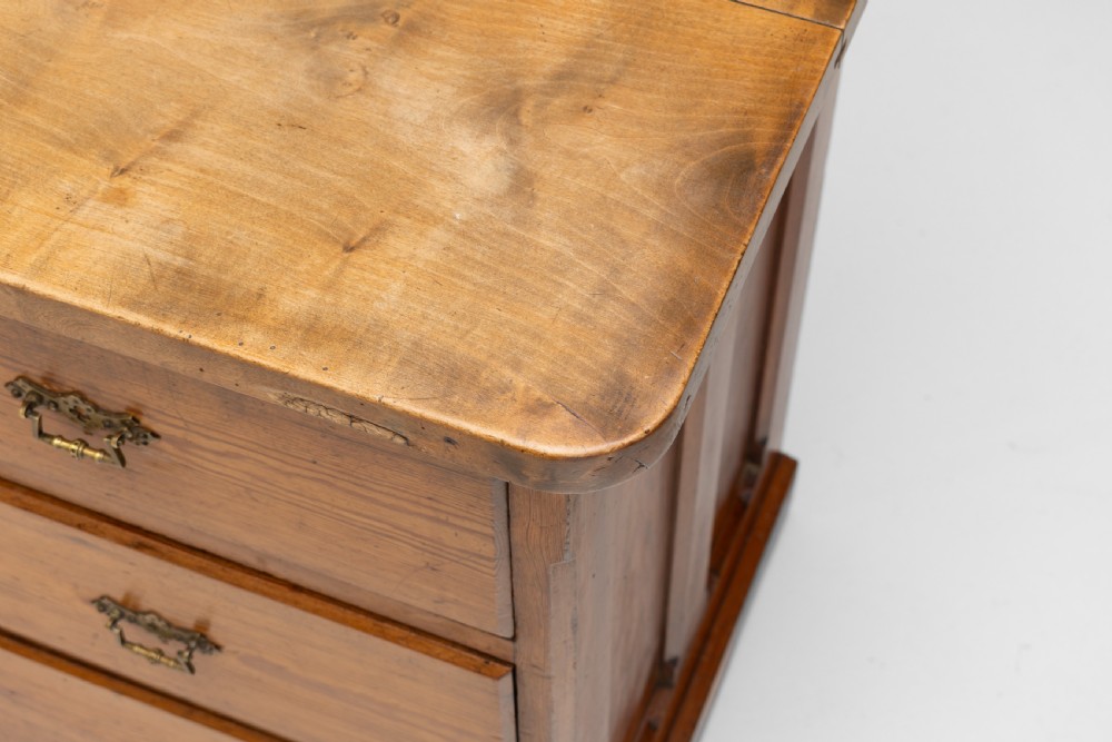 A warm brown pine sideboard featuring a central arched cupboard door flanked by six drawers with brass handles on a solid plinth base. View XII