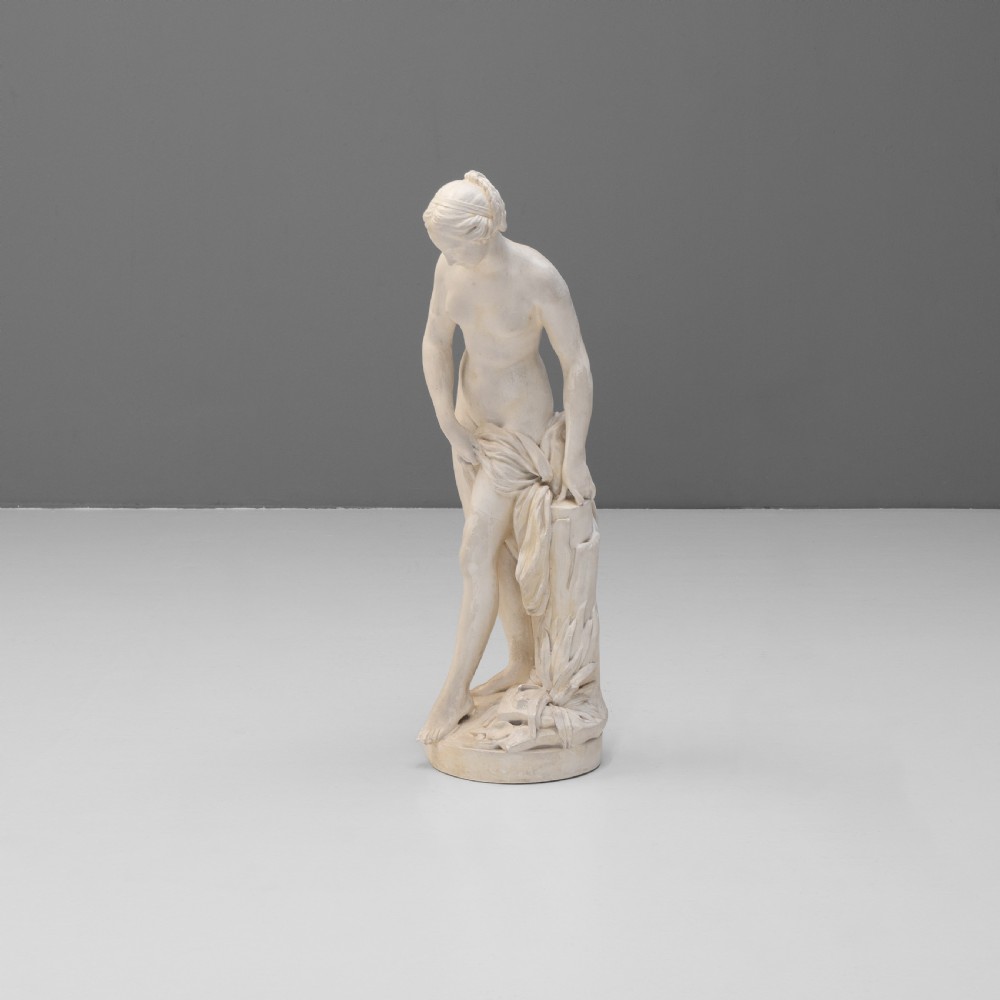 An off-white Neoclassical standing female bather sculpture draped in cloth on a circular base.