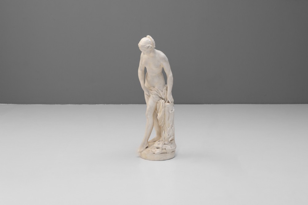 An off-white Neoclassical standing female bather sculpture draped in cloth on a circular base. View II