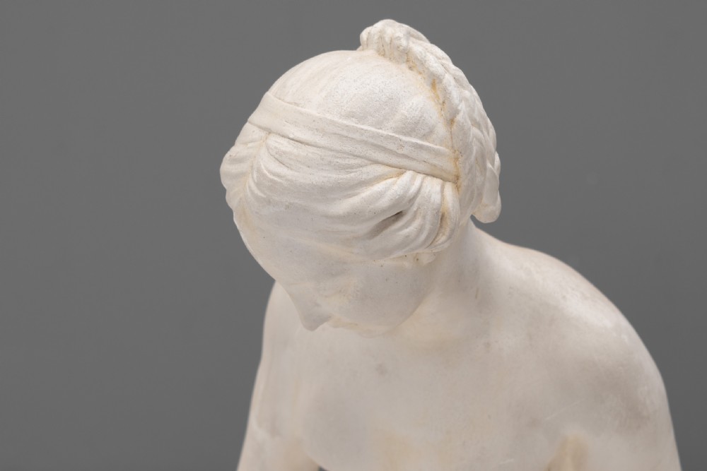 An off-white Neoclassical standing female bather sculpture draped in cloth on a circular base. View III