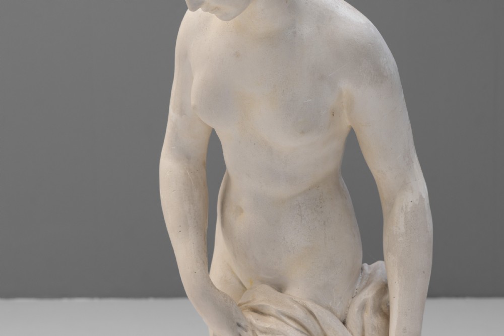 An off-white Neoclassical standing female bather sculpture draped in cloth on a circular base. View IV