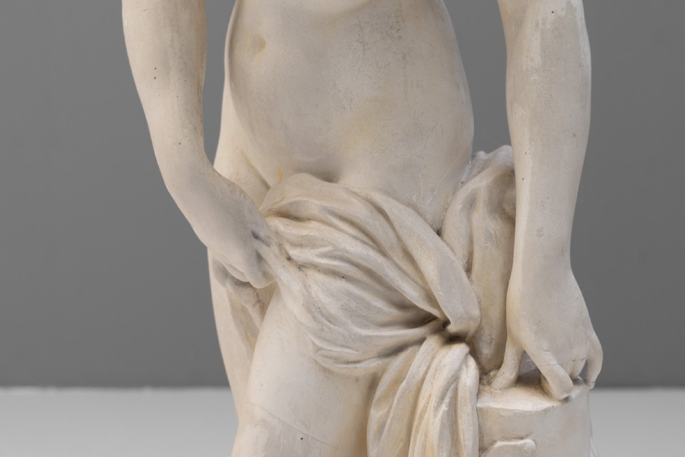 An off-white Neoclassical standing female bather sculpture draped in cloth on a circular base. View V