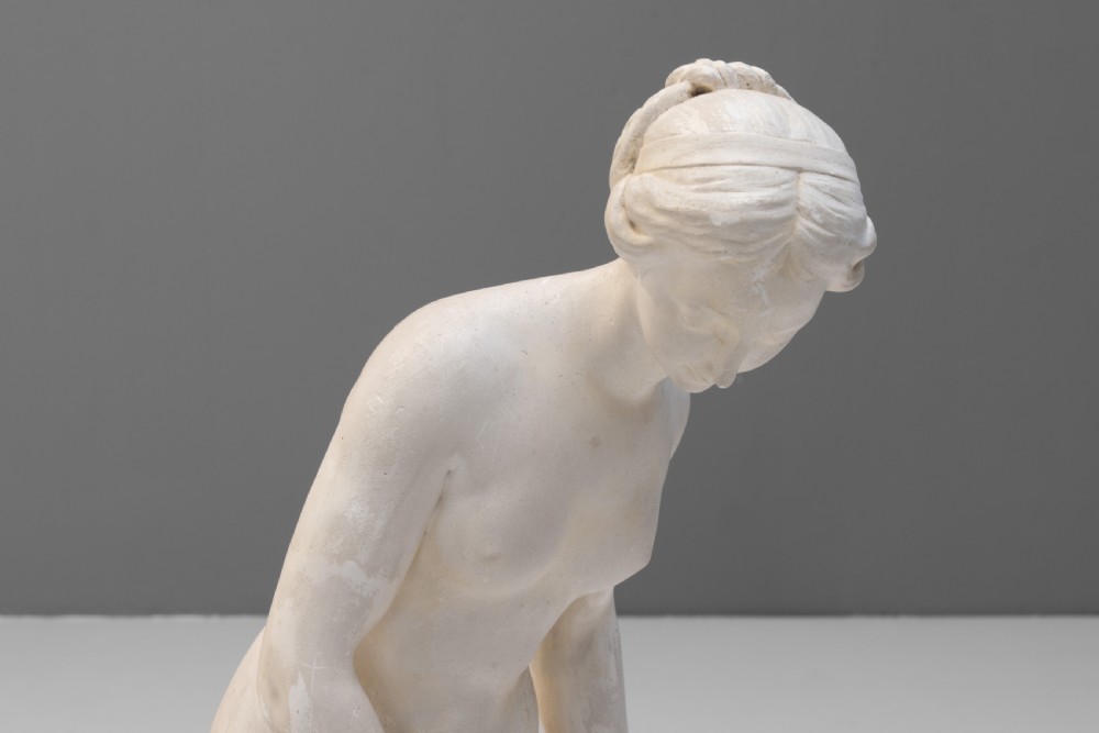 An off-white Neoclassical standing female bather sculpture draped in cloth on a circular base. View VIII