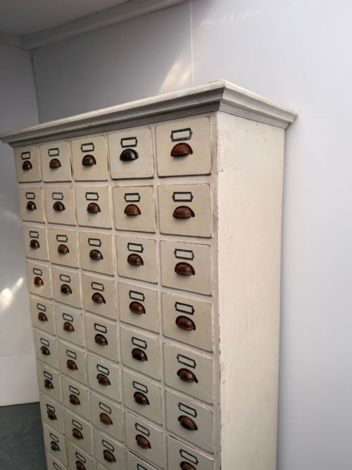 fig 1. A tall off-white painted pine cabinet featuring fifty individual drawers with dark metal shell handles and label holders.