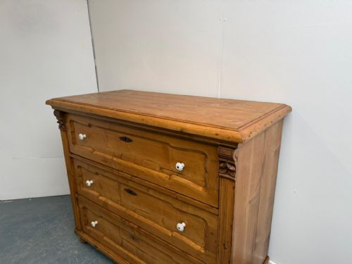 fig 1. A waxed pine chest of drawers featuring three wide drawers with shaped panel details and white ceramic handles.