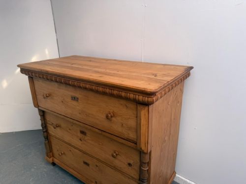 fig 1. A waxed pine chest of drawers featuring three full-width drawers with turned wooden knobs, flanked by carved side columns and topped with carved trim.