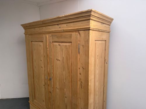fig 1. A freestanding natural pine two-door wardrobe featuring panelled doors, a stepped pediment cornice, and a plinth base.