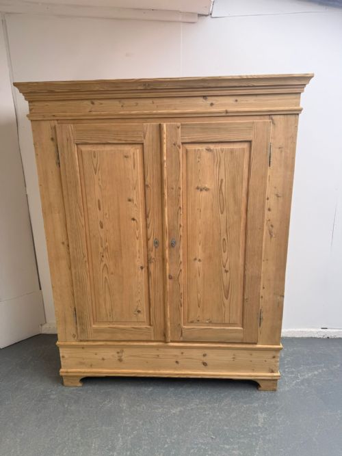 fig 2. A freestanding natural pine two-door wardrobe featuring panelled doors, a stepped pediment cornice, and a plinth base.