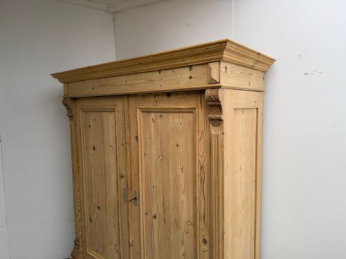fig 2. A Victorian stripped pine two-door wardrobe featuring a knockdown construction, carved corbels, panelled doors, metal escutcheons, and bun feet.