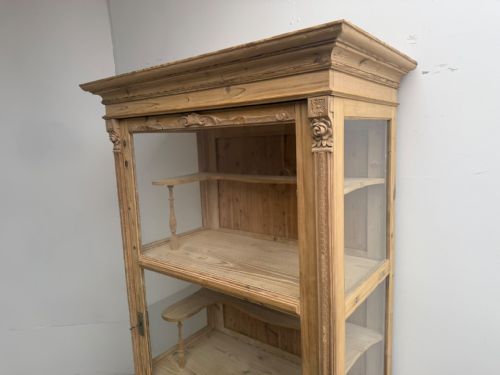 fig 1. A tall Victorian stripped pine display cabinet with glass front and side panels, carved corner detail, and interior timber shelving.