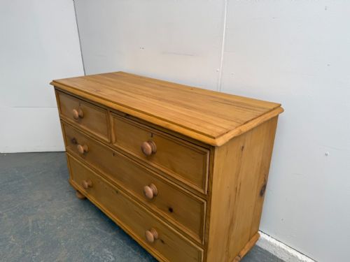 fig 1. A low and wide Victorian waxed pine chest of drawers featuring two short drawers over two long drawers with turned wooden knobs and bun feet.