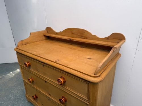 fig 1. An early Victorian waxed pine chest of drawers featuring three wide drawers with turned wooden knobs and a shaped gallery upstand.
