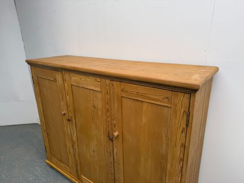 fig 1. A large Victorian waxed pine storage cupboard featuring panelled doors and turned wooden knobs on a low plinth base.