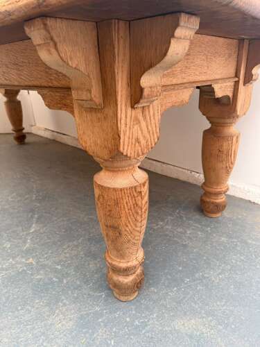 fig 2. A large Victorian golden oak dining table featuring a thick rectangular top with rounded corners and four turned wooden legs.