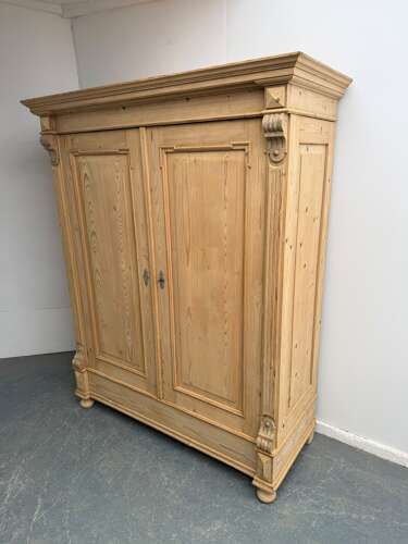 A double-door Victorian stripped pine wardrobe featuring carved corbels, moulded door panels, and turned bun feet.