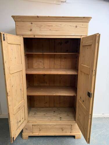fig 2. A tall Georgian natural pine wardrobe featuring two fielded panel doors, a deep moulded cornice, a single base drawer, and turned wooden knobs.