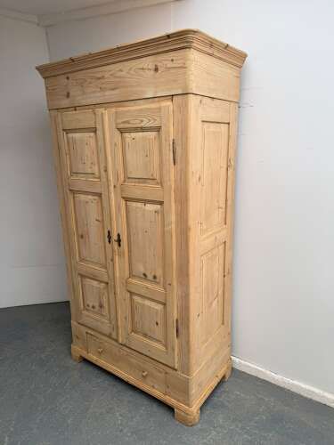 A tall Georgian natural pine wardrobe featuring two fielded panel doors, a deep moulded cornice, a single base drawer, and turned wooden knobs.