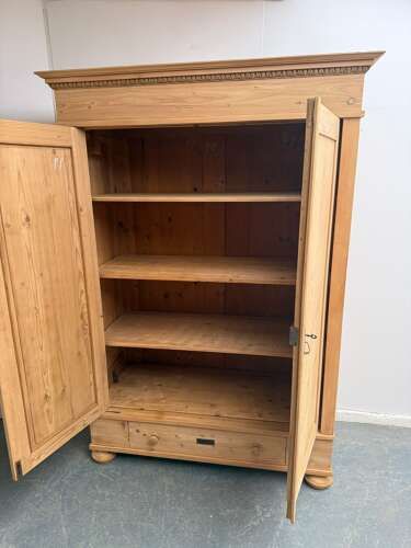 fig 2. A Victorian stripped pine two-door wardrobe featuring a carved dentil cornice, panelled doors, a bottom drawer, and turned feet.