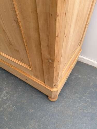 fig 2. A tall stripped pine double-door cupboard featuring a moulded top cornice, panelled doors, and turned bun feet.