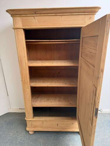 fig 1. A single-door antique stripped pine wardrobe featuring recessed panel detailing, a flared top cornice, an iron keyhole, and flattened bun feet.