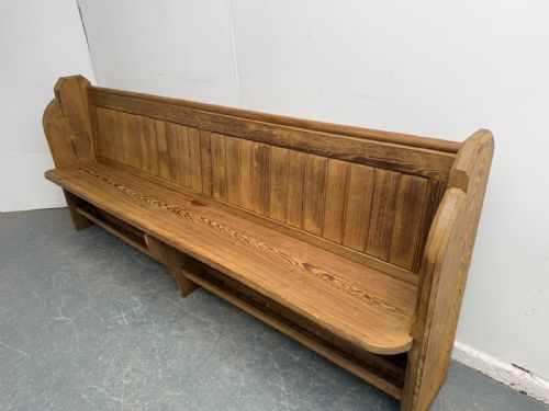 fig 1. A long Victorian pine church pew featuring a vertical panelled backrest, shaped end supports, and an under-seat rack.