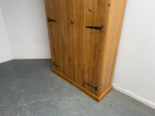 fig 1. A tall solid pine storage cupboard with two planked doors, black iron strap hinges, and a small brass knob.